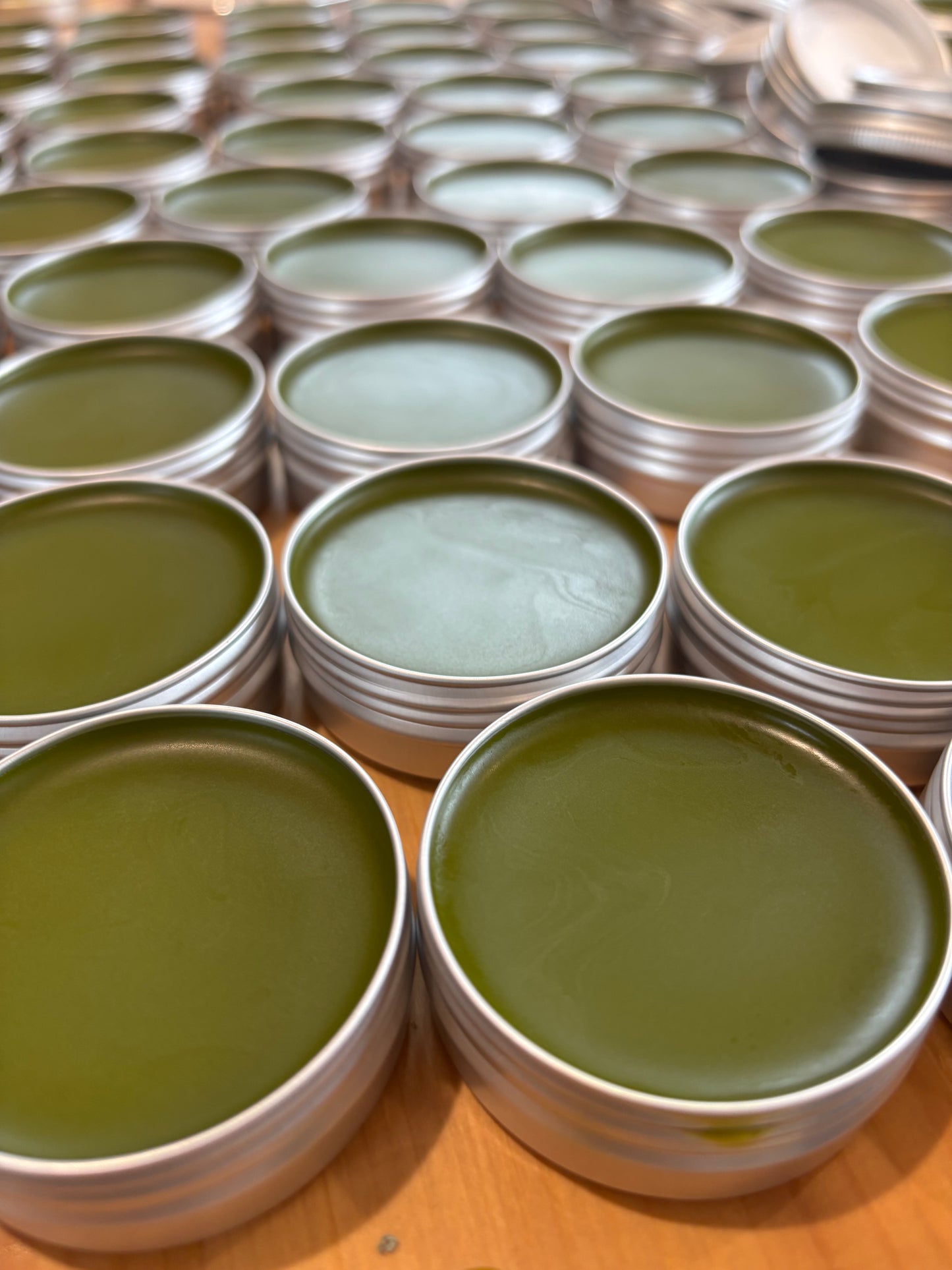 Open tins of our herbal salve, showing a glowing green color. The salve is made with calendula, comfrey, goldenrod, gotu kola, and echinacea.