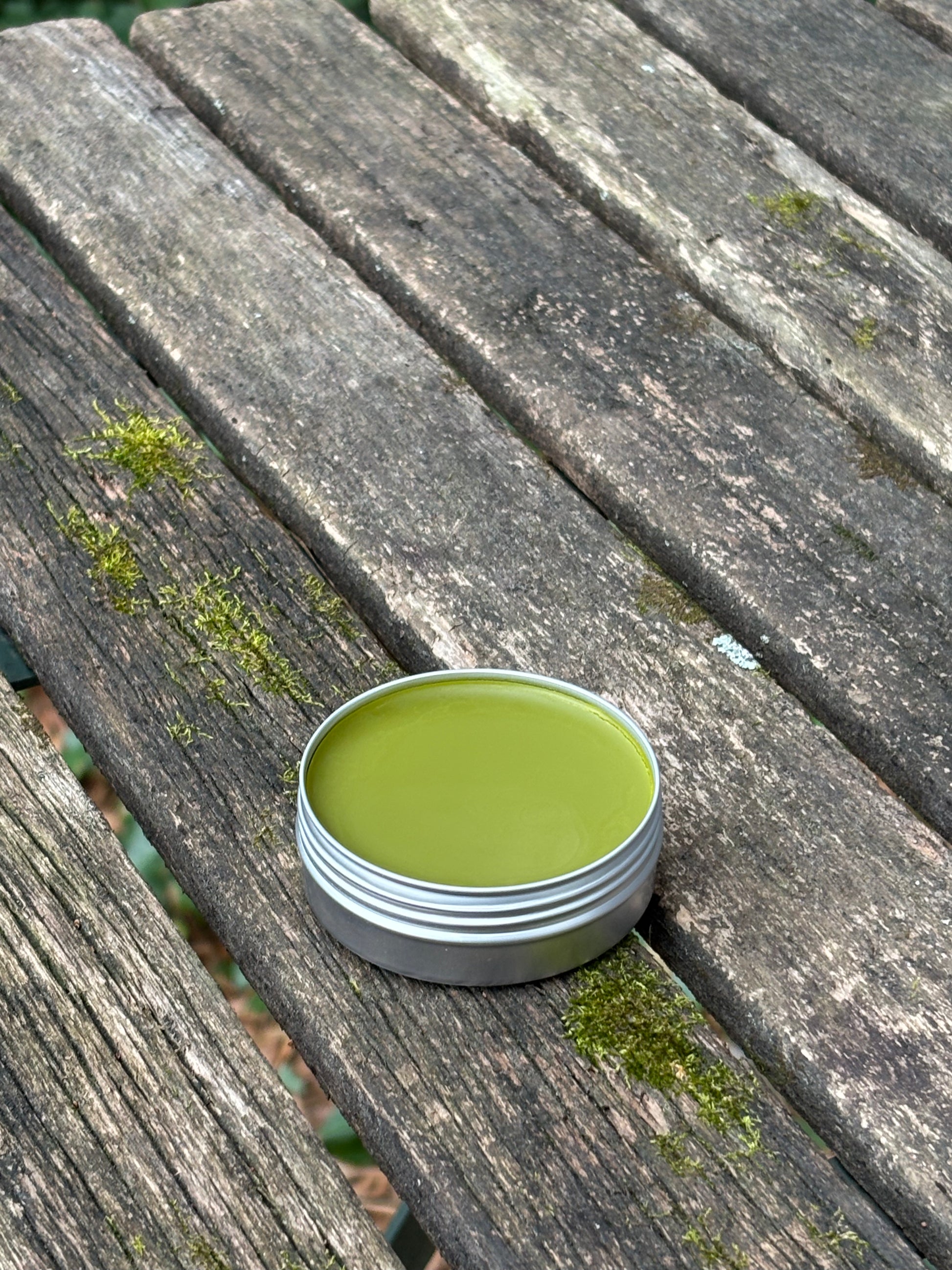 An open two ounce tin of our herbal salve for healing wounds, burns, rashes, and more, featuring calendula, comfrey, goldenrod, gotu kola, and echinacea